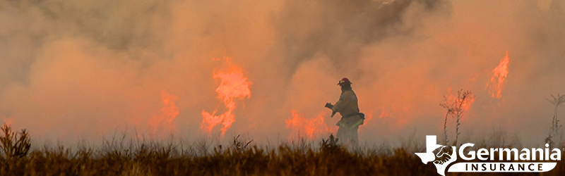 A firefighter standing in the grass in front of a Texas wildfire