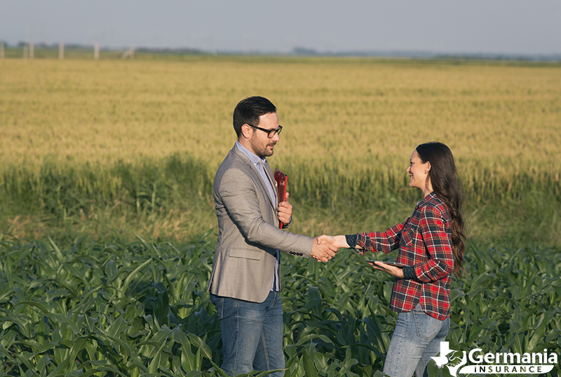 A Texas farmer shaking hands in a field with a farm and ranch insurance agent.