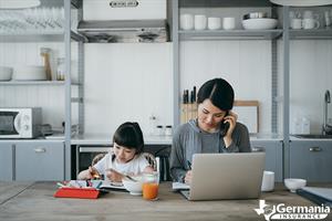 A woman working at her home business next to her daughter