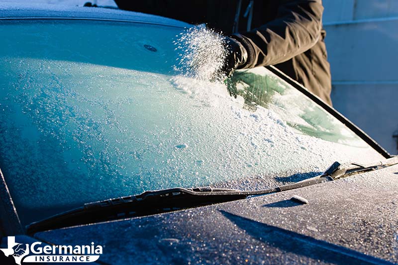 A man performing winter windshield maintenance by removing ice from his windshield